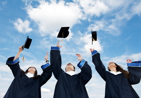 three graduate students tossing up hats over blue sky